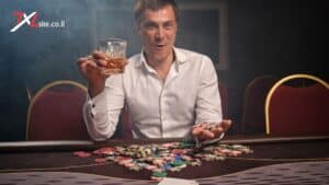 7XL POKER - שחקן קזינו מחזיק כוס משקה וז׳יטונים צבעוניים ליד שולחן פוקר עמוס בז׳יטונים, על רקע אולם אפוף עשן וכיסאות אדומים.